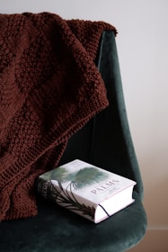 A cozy knitted blanket draped over a chair with a pattern booklet beside it.