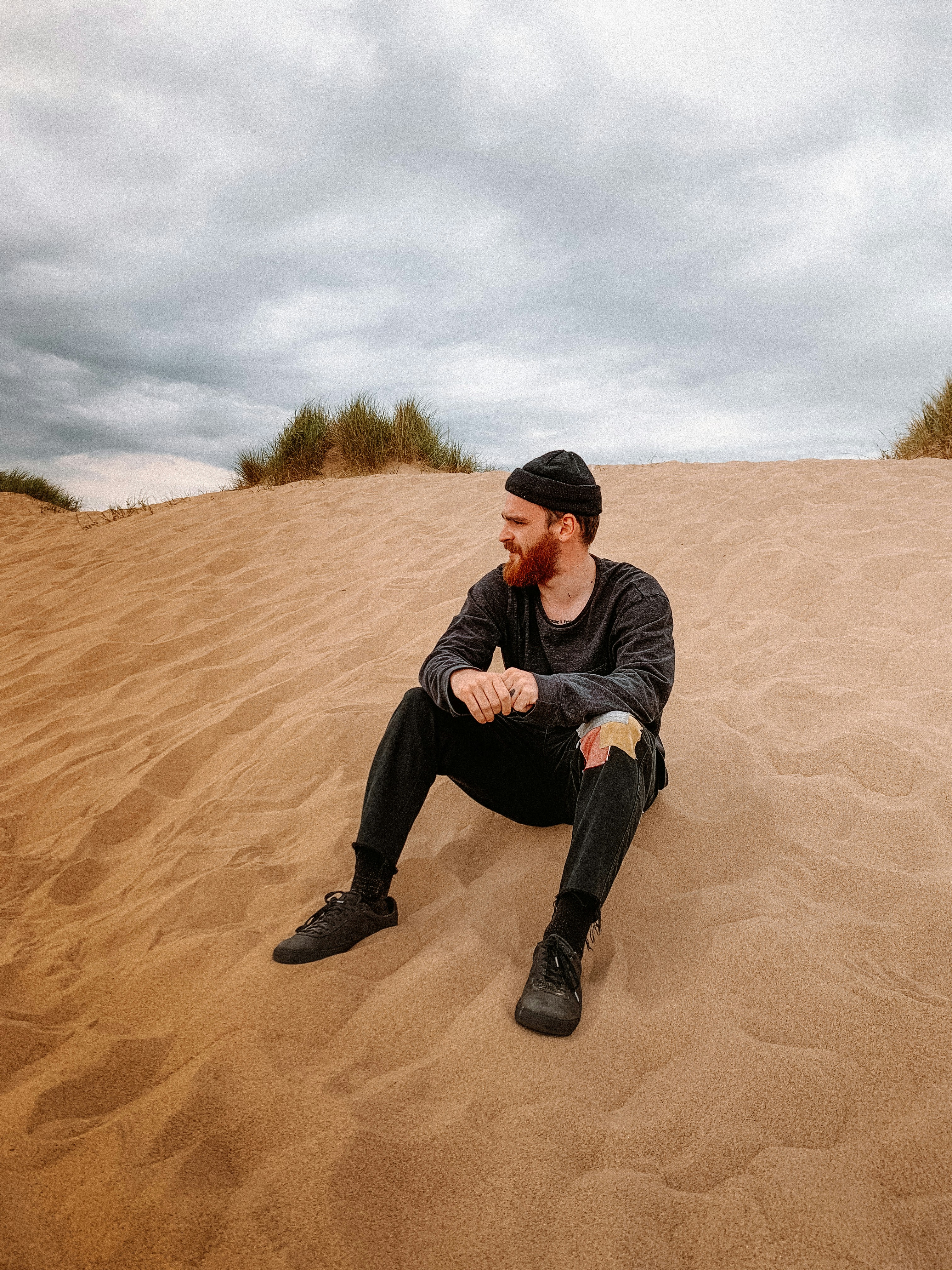 man in black jacket and black pants sitting on brown sand during daytime