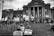 A group of people are gathered on the steps of a large, classical-style building, engaged in a protest. Many are holding signs with messages advocating for justice and equality, such as 'Black Lives Matter', 'No Justice No Peace', and 'End Police Brutality'. The participants appear to be united in their cause, standing on and around the steps with a strong sense of purpose.
