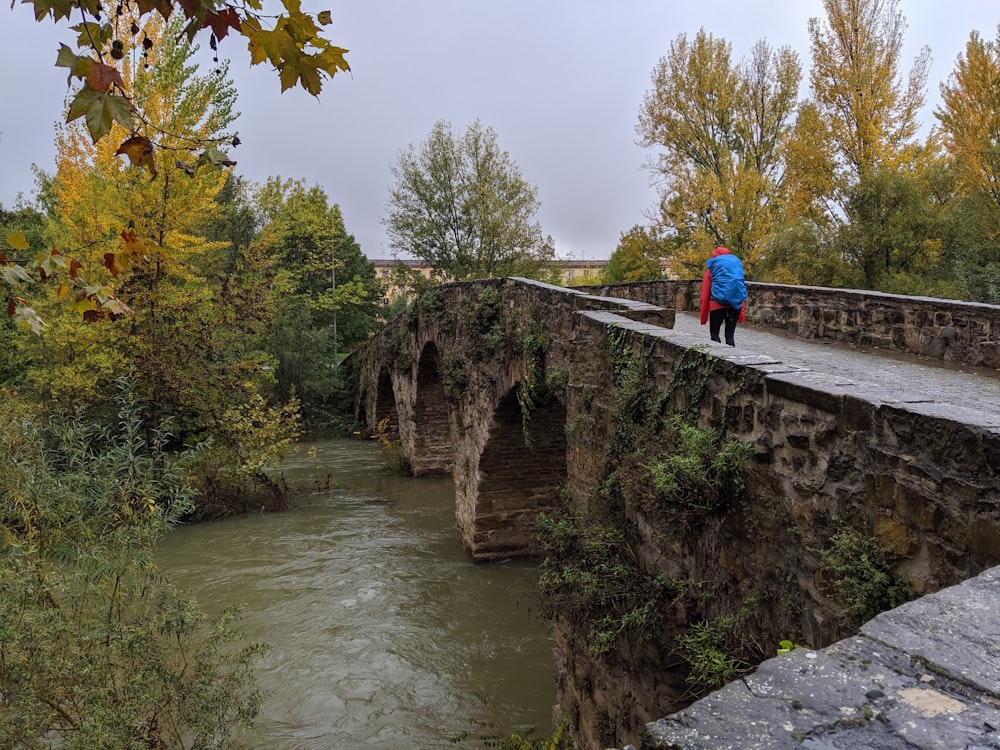 Mann in blauer Jacke geht tagsüber auf Betonbrücke