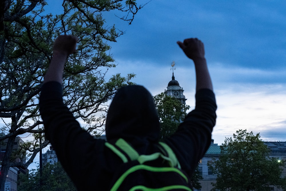 person in black and green jacket raising right hand