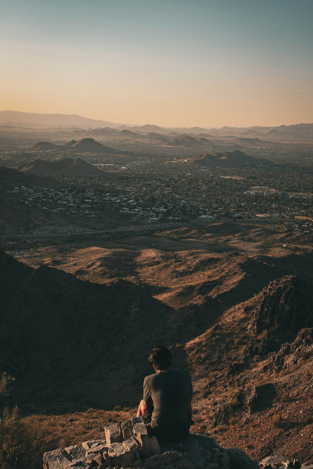 man sitting on rock looking at the mountains during daytime