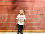 A child in a white pirate t-shirt with black line art, sitting against a concrete wall with black doodles.