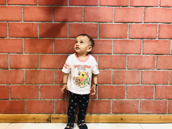 A child in a white pirate t-shirt with black line art, sitting against a concrete wall with black doodles.