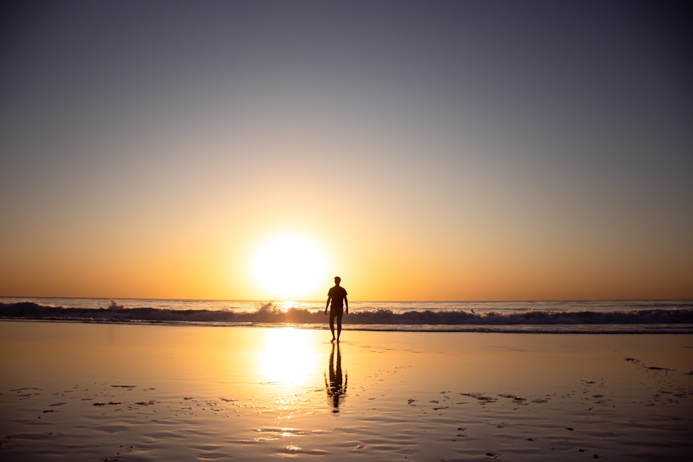 Mujer en vestido negro caminando en la playa durante la puesta del sol