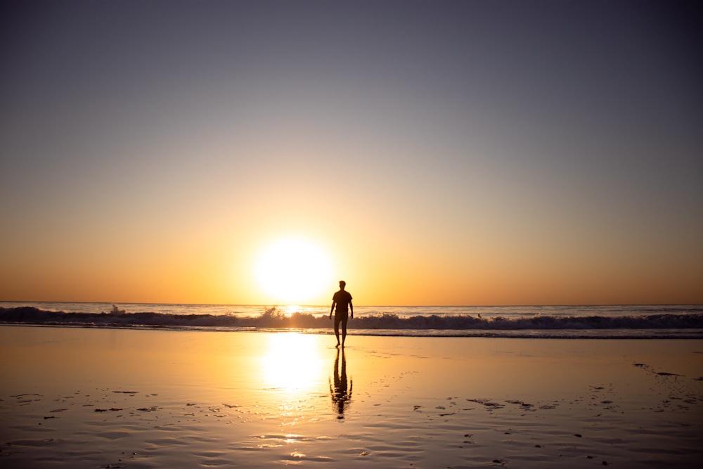 woman in black dress walking on beach during sunset