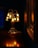 A delicately crafted lamp with multiple bell-shaped glass shades emits a warm, golden glow. The lamp sits on a polished wooden surface, and the rich, dark background adds contrast to the ambient light. The reflection of the lamp's light creates a soft, inviting atmosphere.