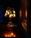 A delicately crafted lamp with multiple bell-shaped glass shades emits a warm, golden glow. The lamp sits on a polished wooden surface, and the rich, dark background adds contrast to the ambient light. The reflection of the lamp's light creates a soft, inviting atmosphere.