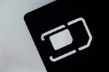 An abstract close-up of a SIM card slot icon, featuring bold, geometric lines and shapes. The negative space is emphasized with a contrasting light gray background and dark, shadowed interior.