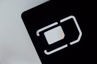 An abstract close-up of a SIM card slot icon, featuring bold, geometric lines and shapes. The negative space is emphasized with a contrasting light gray background and dark, shadowed interior.