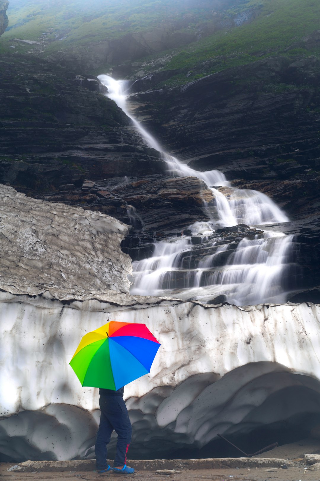 person holding umbrella standing on rock formation near waterfalls during daytime