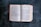An open book with two visible pages showing text from the Bible, specifically the books of Exodus and Leviticus. The book is lying flat on a dark surface with a worn-out red cover.