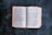An open book with two visible pages showing text from the Bible, specifically the books of Exodus and Leviticus. The book is lying flat on a dark surface with a worn-out red cover.