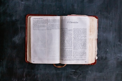 An open book lies on a dark surface, displaying text from 1 Chronicles and 2 Chronicles. The pages are slightly worn, suggesting age or frequent use. The book is centered and takes up most of the image, capturing a sense of focus and contemplation.