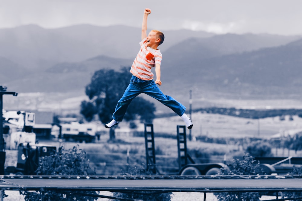 man in white t-shirt and blue denim jeans jumping on black metal railings during daytime