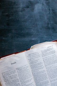 An open Bible displaying the Book of Jonah, with its pages spread and a dark, textured chalkboard surface in the background.