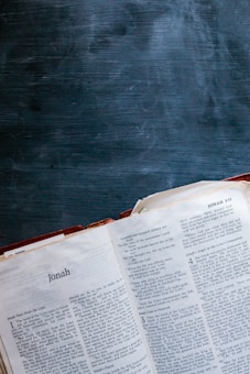An open Bible displaying the Book of Jonah, with its pages spread and a dark, textured chalkboard surface in the background.