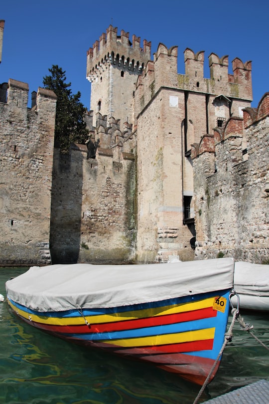 white yellow and blue boat on body of water near brown concrete building during daytime in Rocca Scaligera Italy