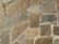 A textured stone wall composed of large, irregularly shaped stones in varying shades of brown, gray, and beige. The stones are fitted together with cement, creating a rugged and natural appearance.