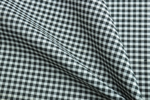 A close-up of a fabric featuring a black and white checkered pattern. The fabric is slightly wrinkled and folded, creating subtle shadows and texture variation.
