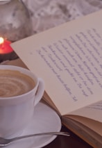 Close-up of a steaming cup of coffee next to an open book in the library corner.