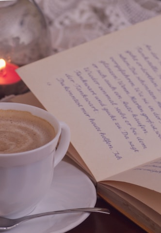 Close-up of a steaming cup of coffee on a wooden table next to an open book.