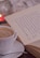 A close-up of a steaming cup of tea next to a cozy book and a candle.
