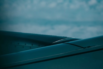 The image features a close-up view of an airplane wing against a backdrop of a cloudy sky, with the metal surface of the wing appearing sleek and polished under the light.