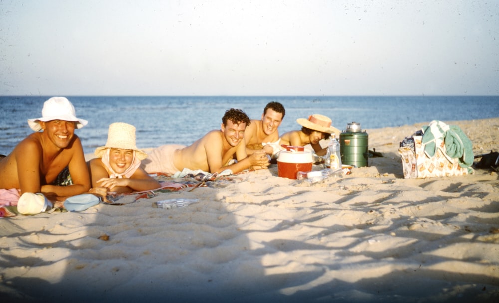 3 women sitting on sand near body of water during daytime
