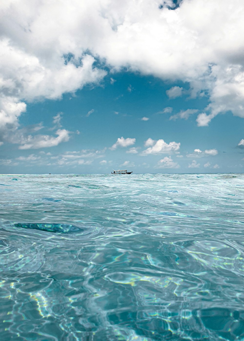 昼間の青空と白い雲の下、海上に浮かぶ白いボート