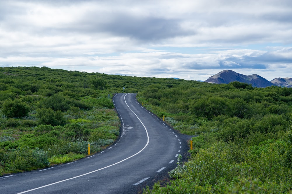 gray concrete road between green grass field under white clouds during daytime