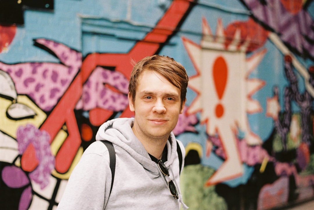 smiling boy in gray hoodie standing near blue and red wall during daytime