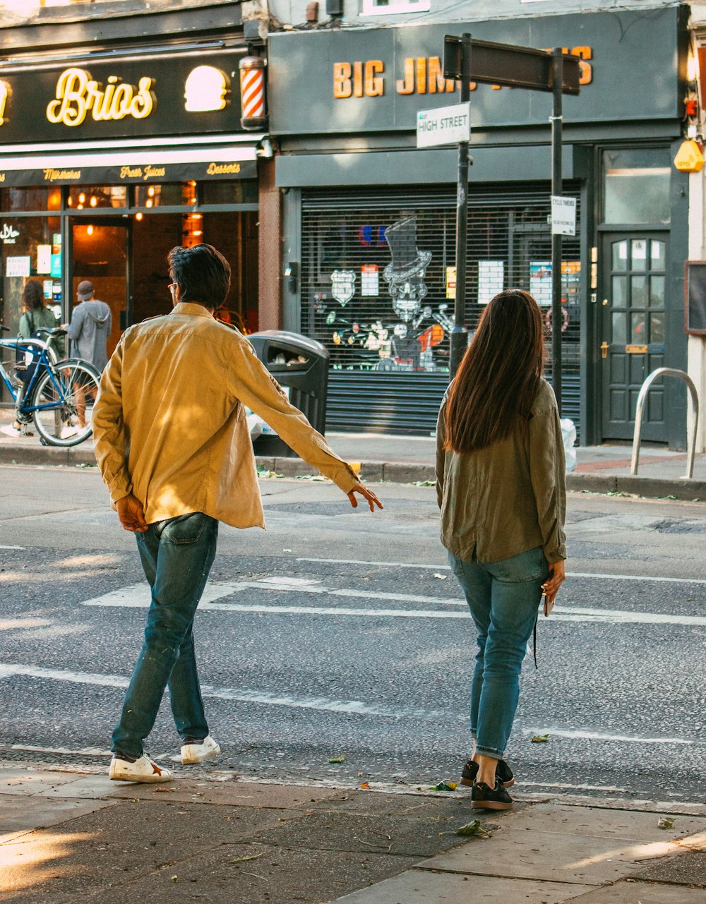 woman in brown jacket and blue denim jeans walking on sidewalk during daytime