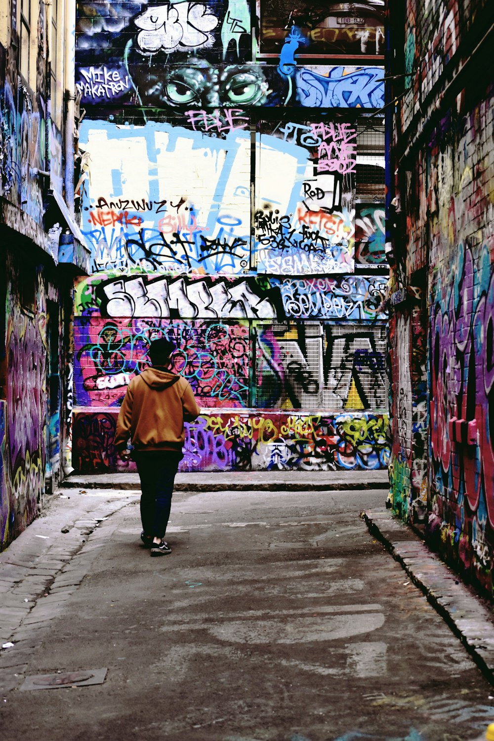 woman in yellow jacket and black pants standing in front of graffiti wall