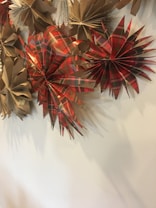 Origami-like decorations made from brown and red plaid paper are displayed against a light-colored wall. The papers are folded into starburst shapes, creating a festive and artistic presentation.