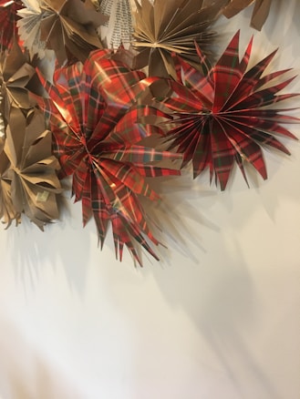 Origami-like decorations made from brown and red plaid paper are displayed against a light-colored wall. The papers are folded into starburst shapes, creating a festive and artistic presentation.