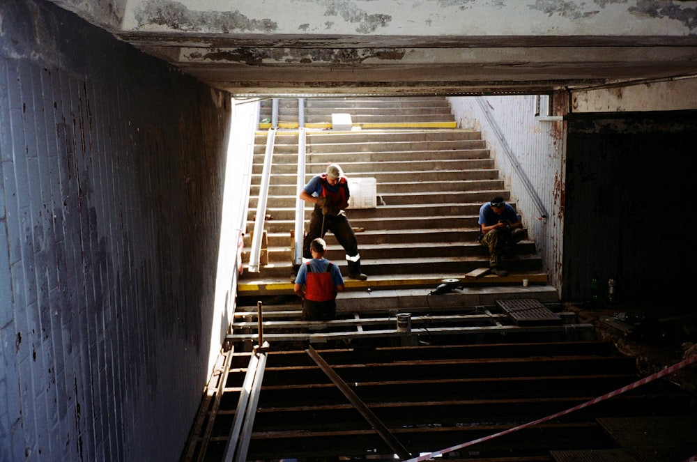 man in orange t-shirt and black pants sitting on brown wooden stairs