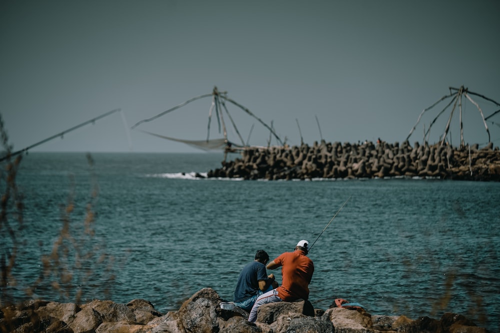 man in orange shirt sitting on rock near body of water during daytime