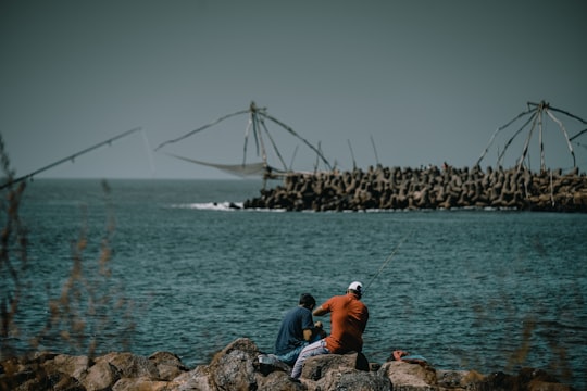 man in orange shirt sitting on rock near body of water during daytime in Kerala India