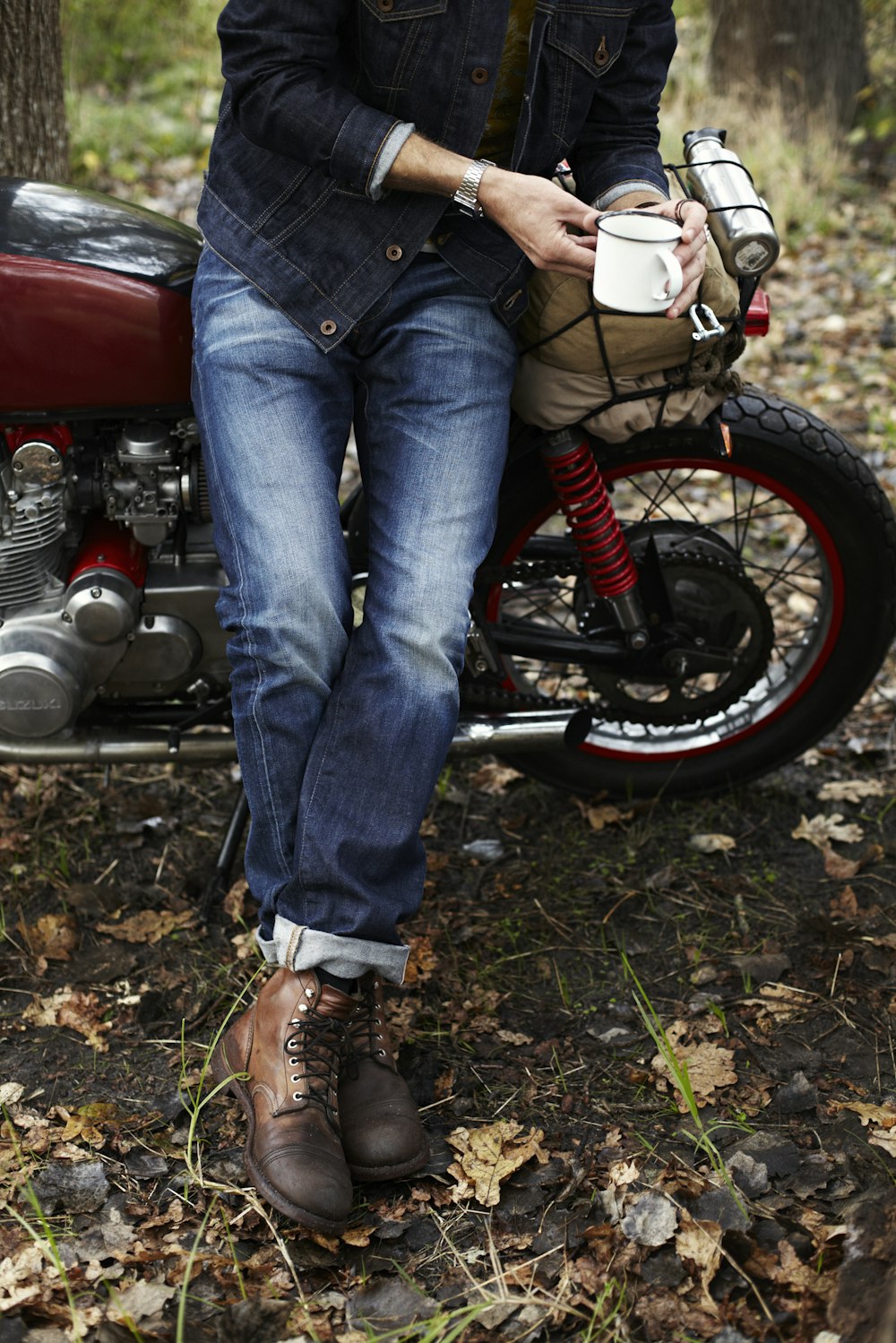 pessoa em jeans azuis e tênis brancos sentados na motocicleta vermelha