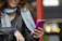 A stylish young woman holding her phone with a blush pink luméa case, smiling in natural light.