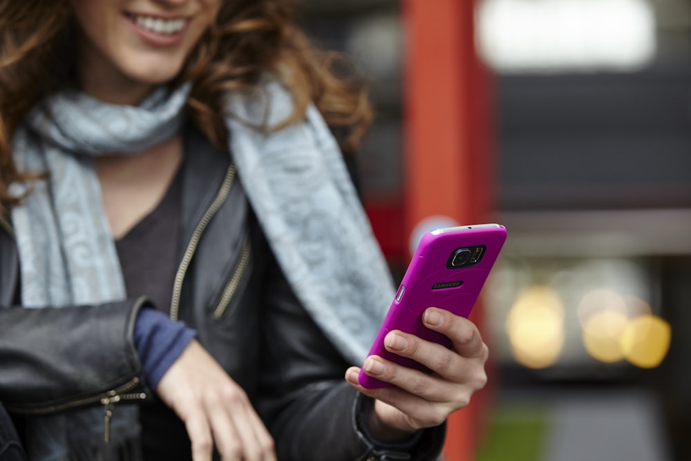 smiling woman in black leather jacket holding purple smartphone