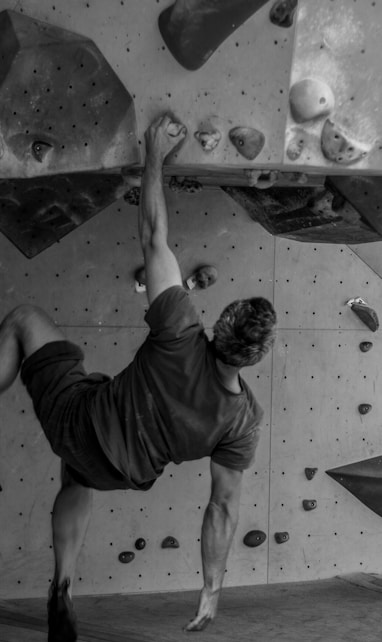 grayscale photo of man in t-shirt and shorts climbing on wall