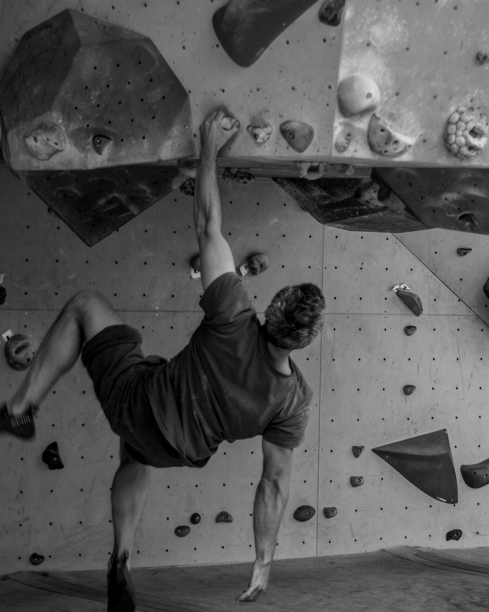 grayscale photo of man in t-shirt and shorts climbing on wall
