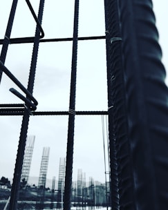 Metal rebar structures stand vertically, forming a framework against a pale sky. In the background, additional rebar formations are visible, likely part of a construction site. The image conveys a sense of industrial progress and development.