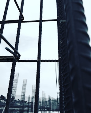 Metal rebar structures stand vertically, forming a framework against a pale sky. In the background, additional rebar formations are visible, likely part of a construction site. The image conveys a sense of industrial progress and development.