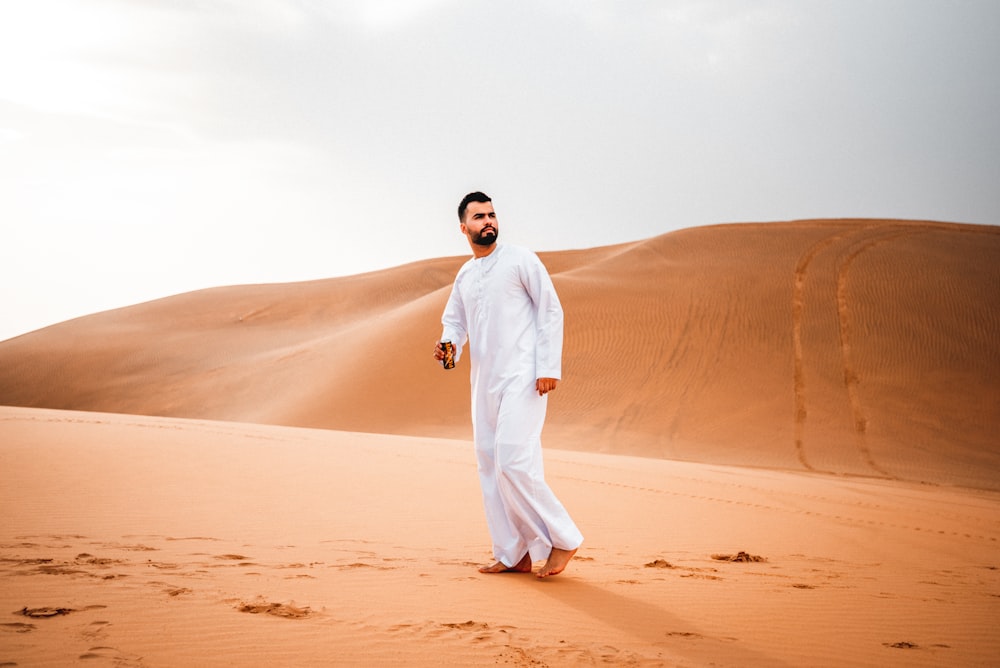 man in white thobe standing on brown sand during daytime