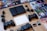 A collection of PlayStation 2 gaming items spread out on a wooden surface includes the console, multiple game discs with cases arranged in a semi-circle, two black controllers, a memory card, various cables, and an instruction manual.