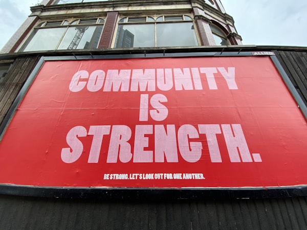 a sign with a red background and white letters reading "Community is Strength. Be strong. Let's look out for one another." 