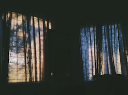 A whisper of silk fabric draping a shadowed room with golden candlelight flickering.